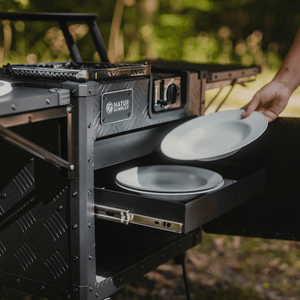 Jemand platziert einen weißen Porzellanteller in der Schublade einer schwarzen Outdoorküche