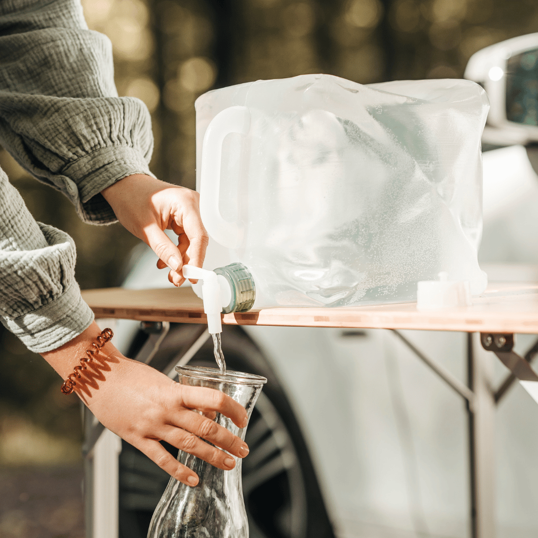 Jemand zapft Wasser aus einem Kanister und lässt es in eine Karaffe laufen. 